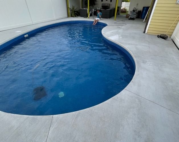 Same kidney pool after its off-season remodel, new liner full of deep blue water behind a brand-new concrete deck