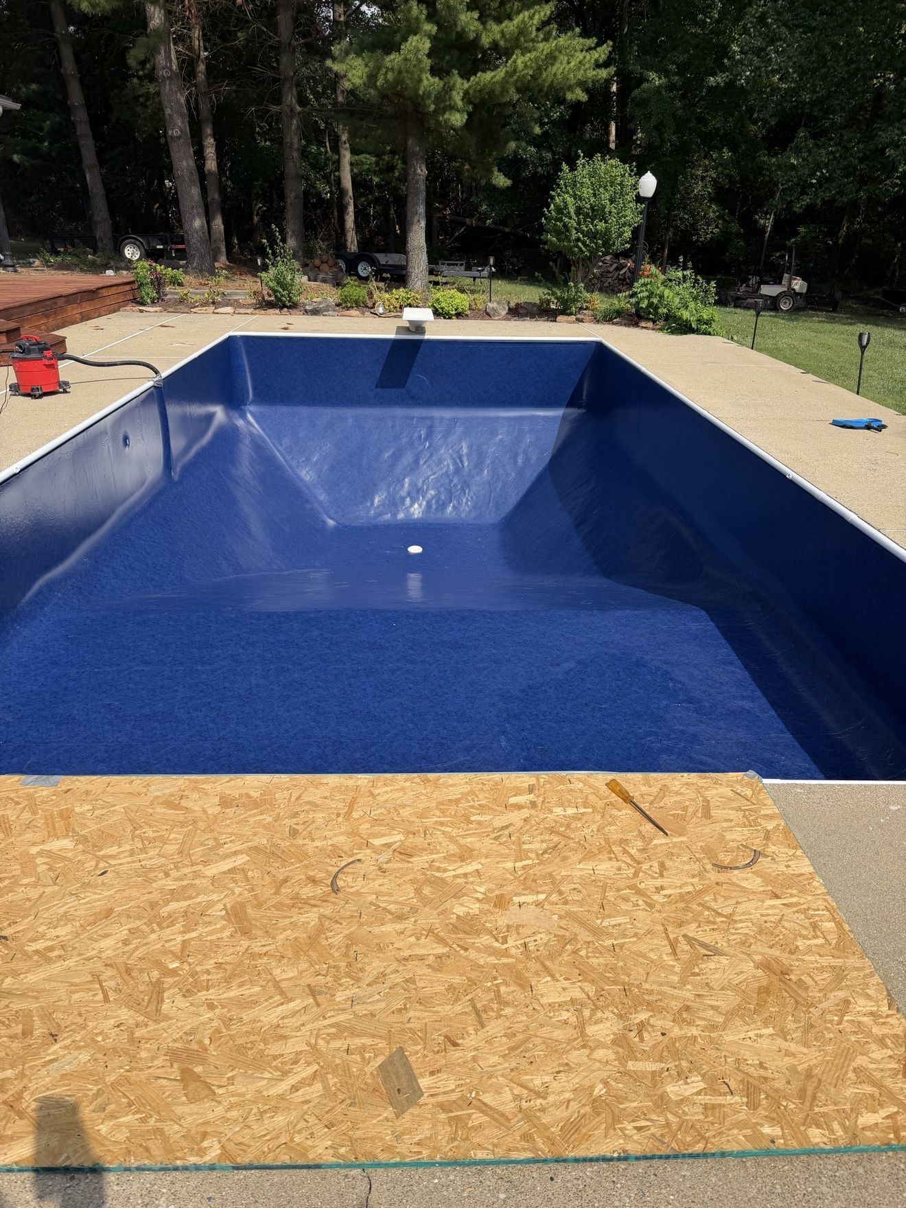 New deep-blue vinyl liner being set in an inground pool with a vacuum pulling it tight