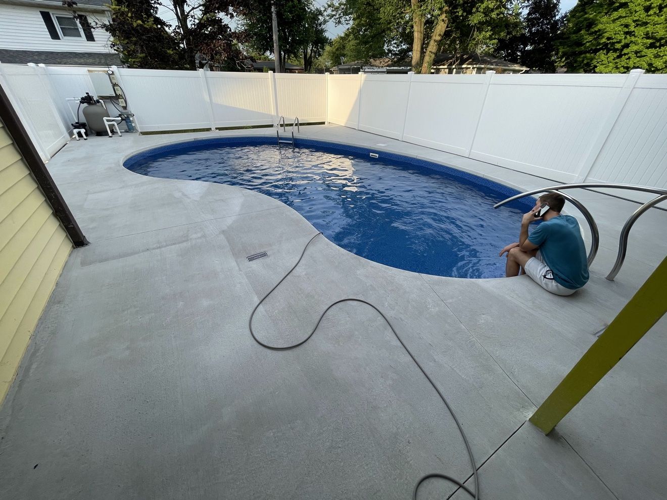 Kidney pool after liner replacement, filled with blue water behind a new concrete deck