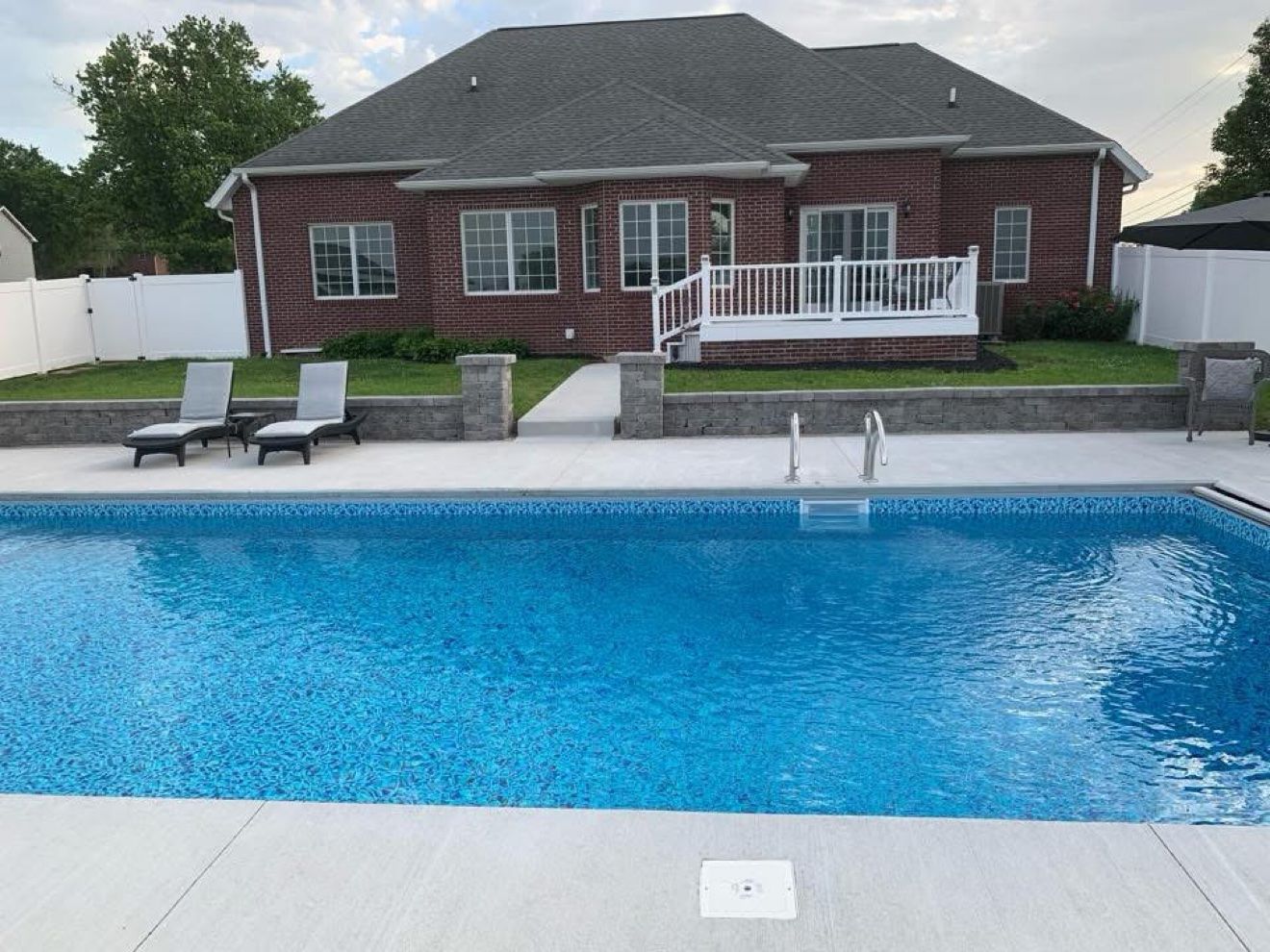 Block retaining wall with pillars behind a Fattys Pools inground pool and concrete deck