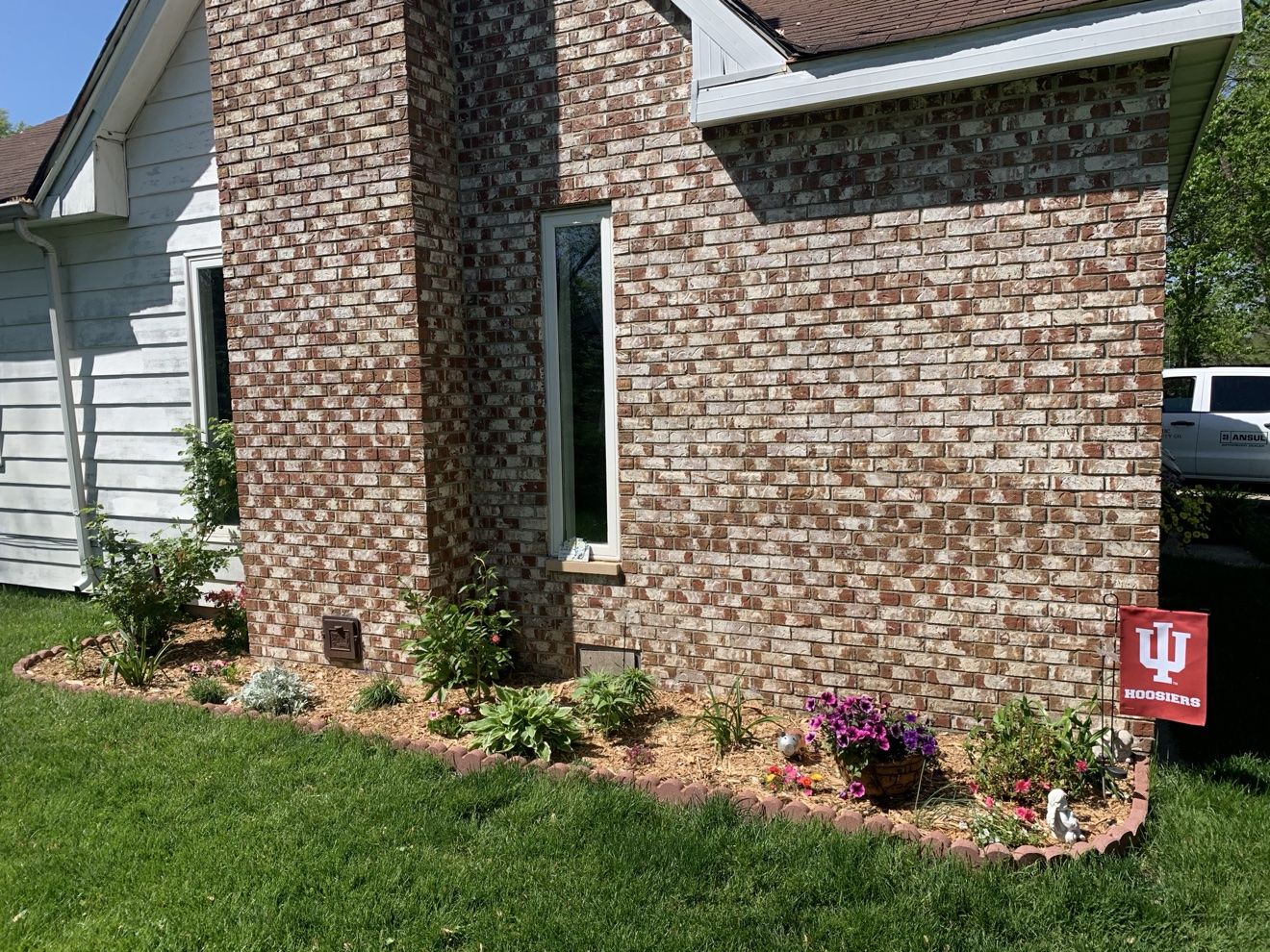 Finished flower bed with brick edging, hostas and flowers along a brick house — Fattys Pools landscaping