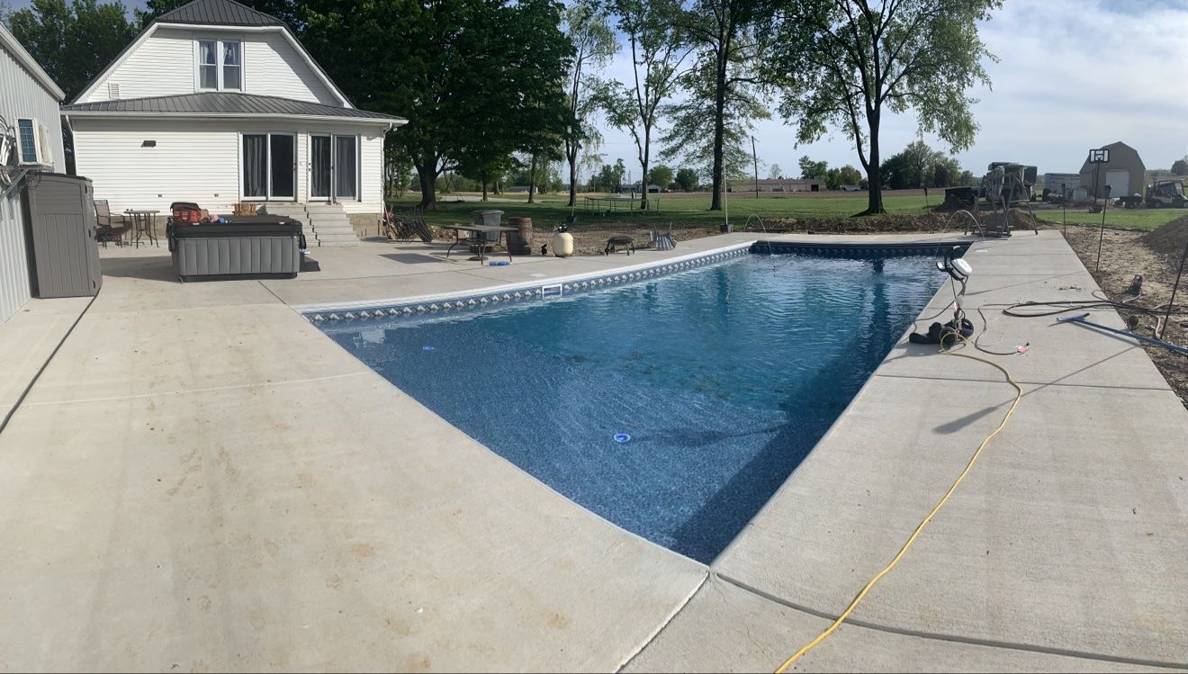 New inground pool build in daylight with a big concrete deck in front of a white farmhouse
